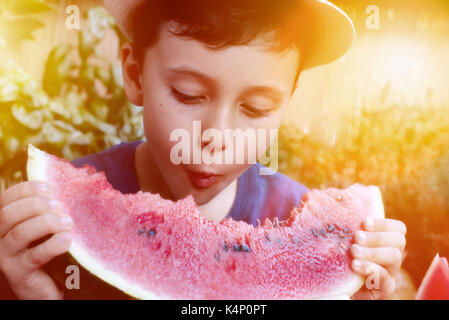 Garçon enfant mignon avec le panama tasse manger sain Aliments biologiques, pastèque. fond nature, feux de soleil Banque D'Images