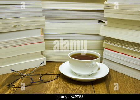 Lunettes de lecture et une tasse de thé à côté de piles de livres et romans. Banque D'Images