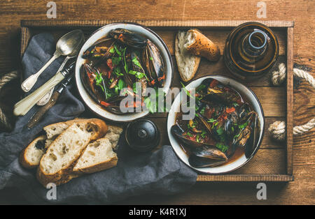 Télévision à jeter des moules bouillies belge à la sauce tomate avec du persil dans les cuves métalliques servant de plateau en bois, des tranches de baguette de pain et de bière light plus de Banque D'Images