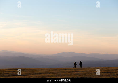 Un couple au sommet d'une montagne à près de coucher du soleil, avec des tons chauds et doux et des collines et montagnes Banque D'Images