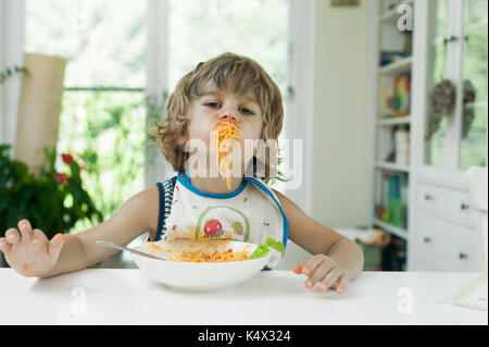 Portrait of a cute jeune garçon faire un gâchis tout en mangeant des pâtes pour le déjeuner Banque D'Images