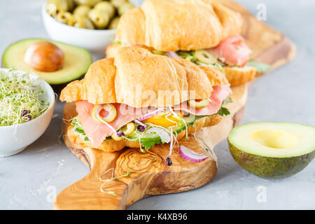 Sandwich croissant avec le poisson, les olives et les légumes sur une planche de bois. Banque D'Images