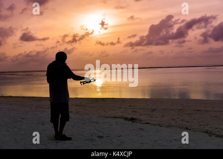 L'homme silhouette le drone de fonctionnement par télécommande sur la plage au Maldives island Banque D'Images