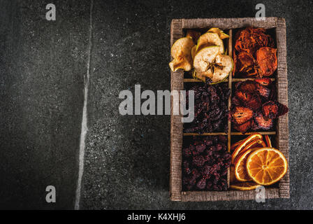 Des baies séchées et les fruits, la récolte pour l'hiver : abricots, pommes, fraises, framboises, cerises, oranges. dans la vieille boîte en bois, sur noir Banque D'Images