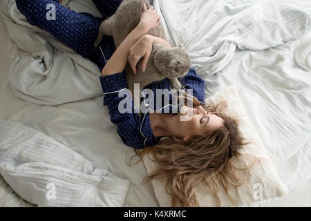 Belle jeune fille en pyjama hugs son chat au lit, vue d'en haut Banque D'Images