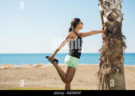 De côté de la sportive en préchauffage leaning against tree Banque D'Images