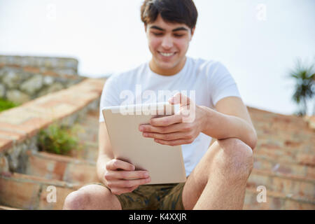 Portrait de jeune homme heureux assis sur des escaliers à l'extérieur à l'aide de tablet Banque D'Images