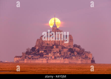 Mont Saint-Michel (Saint Michael's Mount), Normandie, nord-ouest de la France : la lune derrière la montagne au lever du soleil Banque D'Images