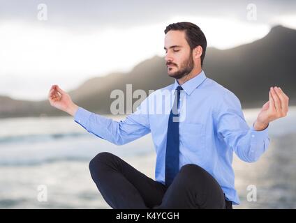 Digital composite of business man meditating contre côte floue Banque D'Images