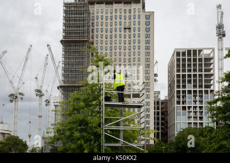 Un wokman portant un gilet hi-vis effectue les réparations à l'éclairage des rues dans Jubilee Gardens, sous de grands bâtiments et Southbank grues de construction, le 6 septembre 2017, à Londres, en Angleterre. Banque D'Images