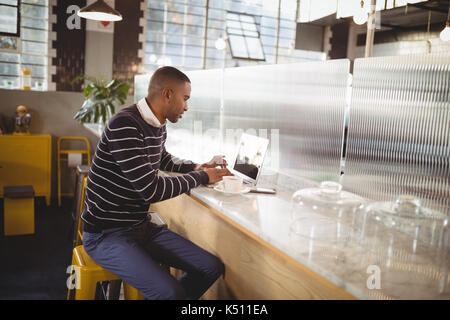 Young male customer typing on laptop while sitting at counter in coffee shop Banque D'Images