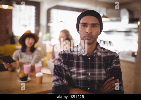 Portrait of young man with arms crossed standing against female friends at coffee shop