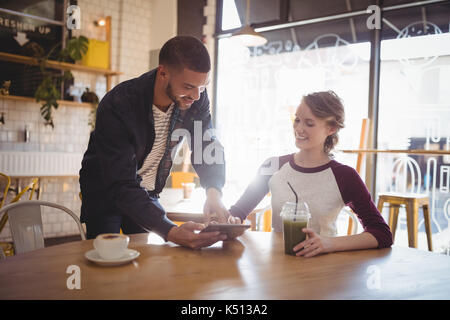 Jeune homme montrant digital tablet to woman at coffee shop Banque D'Images