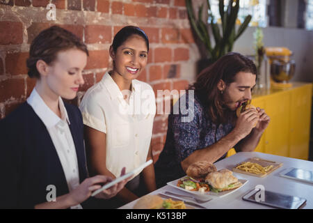 Portrait of smiling young woman sitting au milieu d'amis à table avec de la nourriture dans un café Banque D'Images