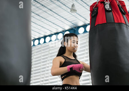 Jeune femme d'exécuter l'exercice dans un centre de remise en forme. athlète féminin de frapper et de sacs de frappe avec une machine à ramer dans la boxe de fitness. sporty girl worki Banque D'Images