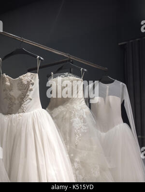 Sélection de robes de mariée blanche fait main accrochée à un rail dans une pièce sombre éclairée par une lumière partiellement Banque D'Images