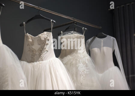 Sélection de robes de mariée blanche fait main accrochée à un rail dans une pièce sombre éclairée par une lumière partiellement Banque D'Images