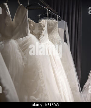 Sélection de robes de mariée blanche fait main accrochée à un rail dans une pièce sombre éclairée par une lumière partiellement Banque D'Images