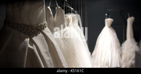 Sélection de robes de mariée blanche fait main accrochée à un rail dans une pièce sombre éclairée par une lumière partiellement Banque D'Images