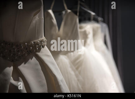 Sélection de robes de mariée blanche fait main accrochée à un rail dans une pièce sombre éclairée par une lumière partiellement Banque D'Images