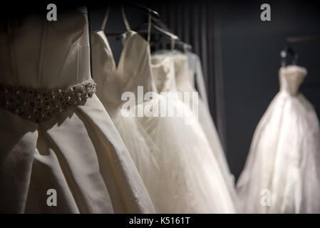 Sélection de robes de mariée blanche fait main accrochée à un rail dans une pièce sombre éclairée par une lumière partiellement Banque D'Images