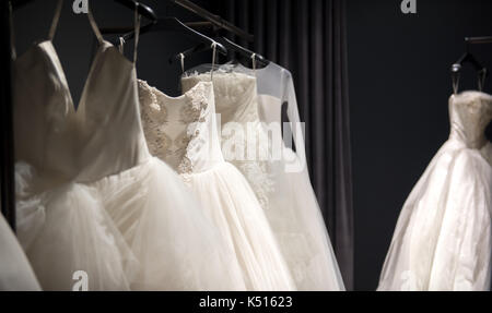 Sélection de robes de mariée blanche fait main accrochée à un rail dans une pièce sombre éclairée par une lumière partiellement Banque D'Images