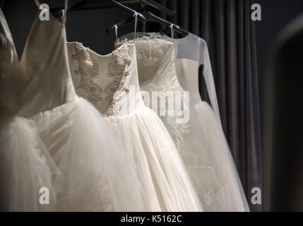 Sélection de robes de mariée blanche fait main accrochée à un rail dans une pièce sombre éclairée par une lumière partiellement Banque D'Images