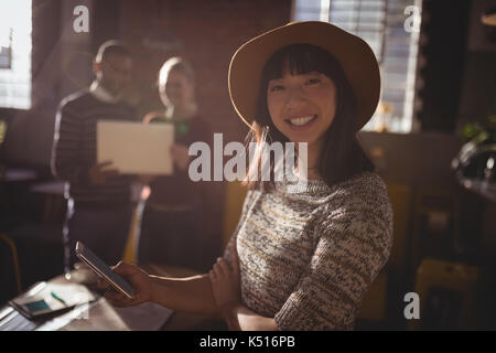 Portrait of smiling woman using smartphone contre collègues article at coffee shop Banque D'Images