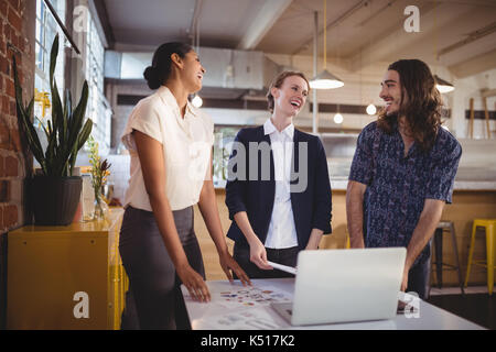 Cheerful young creative team standing par ordinateur portable sur le tableau in coffee shop Banque D'Images