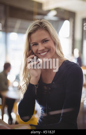 Portrait of smiling young blonde Woman talking on mobile phone while sitting at cafe Banque D'Images