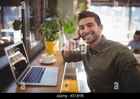 Portrait of smiling young man de tout smartphone at cafe Banque D'Images