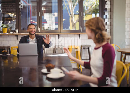 Jeunes amis tout en agitant sitting at table in coffee shop Banque D'Images
