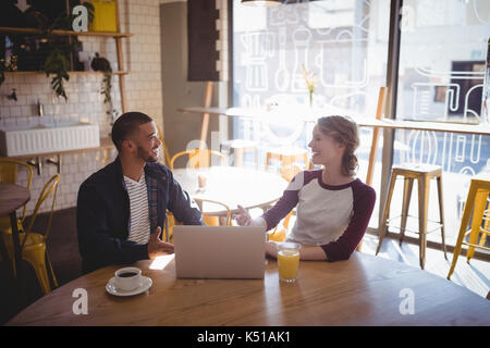 Smiling young friends talking while sitting with laptop at table in coffee shop Banque D'Images