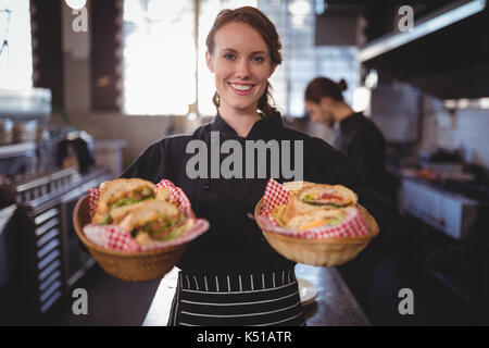 Portrait of smiling waitress servant des hamburgers dans des paniers au café permanent Banque D'Images