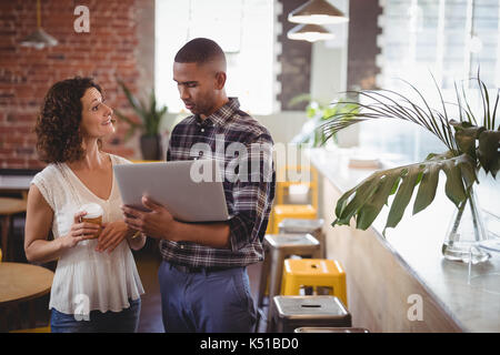 Les jeunes amis parler tout en maintenant l'ordinateur portable et café au café Banque D'Images