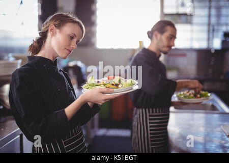 Les jeunes serveurs holding fresh salade Assiettes tout en se tenant dans une cuisine commerciale du coffee shop Banque D'Images