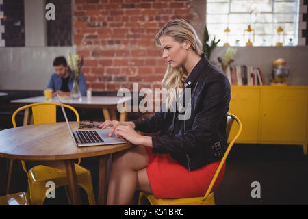 Side view of young blonde woman using laptop while sitting at table in coffee shop Banque D'Images