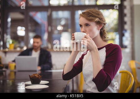 Belle jeune femme de boire du café à partir de la tasse alors que sitting at table in cafe Banque D'Images