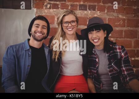 Portrait of smiling young creative team against brick wall at coffee shop Banque D'Images