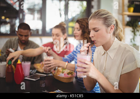 Jeune femme à boire le lait frappé alors qu'il était assis avec des amis au café Banque D'Images