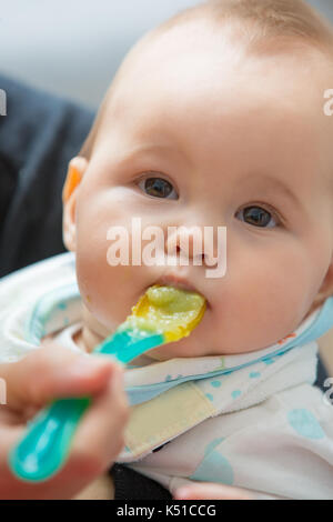 Mère nourrir bébé fille avec la purée d'avocat et de légumes verts, de l'alimentation sur une cuillère en plastique ; le concept de la vie familiale, l'alimentation saine et la nutrition infantile Banque D'Images