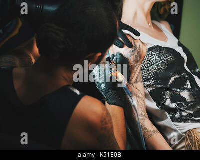 Portrait d'un homme maître de tatouage avec des dreadlocks montrant processus de création tatouage sur le corps féminin sous la lampe de l'artiste travaillant dans sa light.professional Banque D'Images