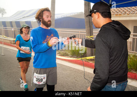 À l'issue d'une course à pied à Huntington Beach, CA, un coureur barbu affiche sa classification code barre pour enregistrer son temps de marche officielle. Note lecteur de code à barres. Banque D'Images