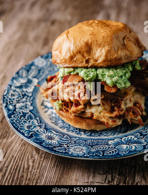 Sandwich au poulet bbq fumé avec oignons sautés, bacon, fromage et jack peper guacamole propagation sur fond rustique Banque D'Images