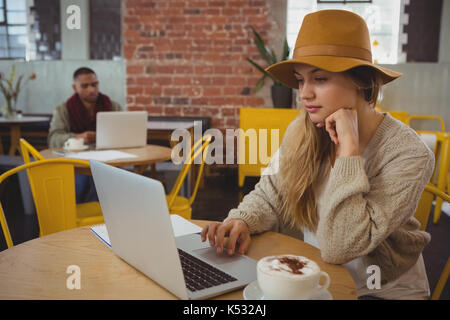 Young businesswoman with coffee cup using laptop at table in cafe Banque D'Images