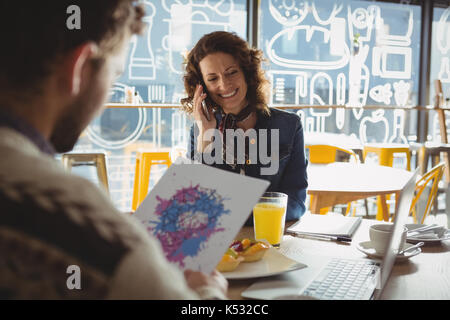 Man holding paper avec peinture de young woman talking on phone in cafe Banque D'Images