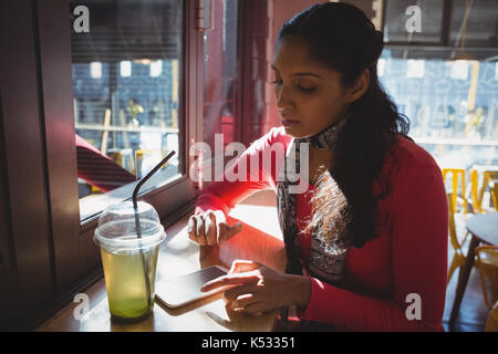 Jeune femme à boire à l'aide de téléphone au rebord de fenêtre dans cafe Banque D'Images
