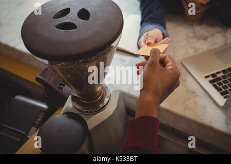 La main coupée de l'homme propriétaire de recevoir le paiement du client par grinder au comptoir de cafe Banque D'Images