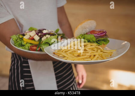 Mid section of waiter holding plaques avec frites et salade in cafe Banque D'Images