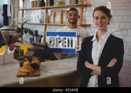 Portrait de femme propriétaire confiant avec waiter holding open sign at counter in cafe Banque D'Images